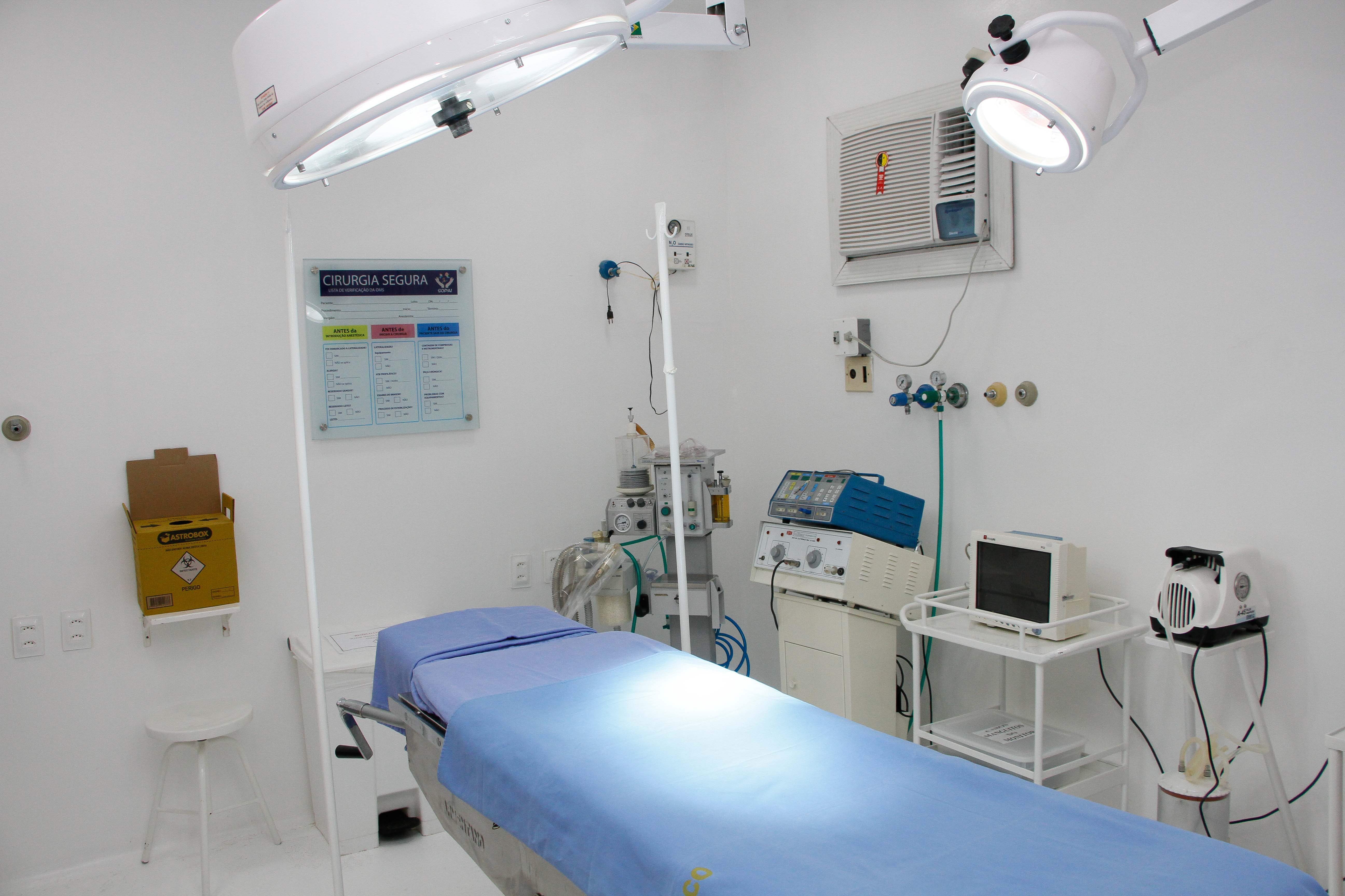 Sala de cirurgia com maca ao meio e equipamentos ao redor