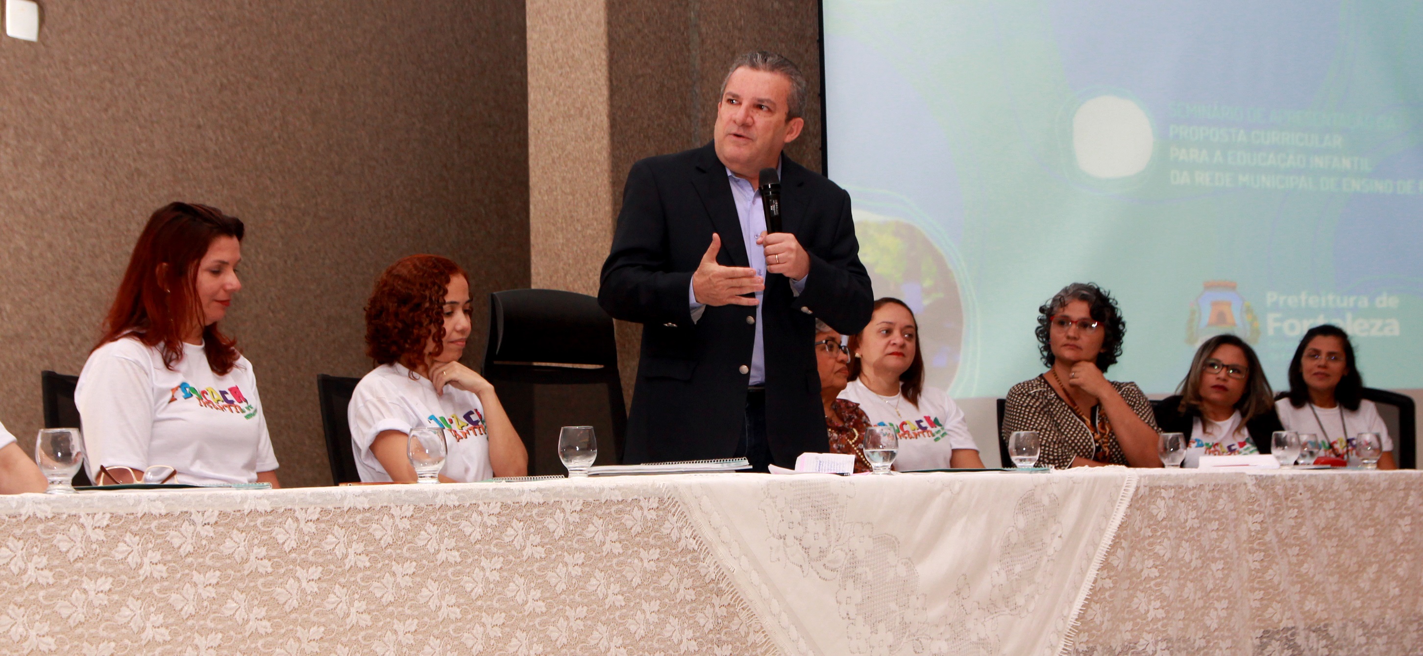 O secretário da Educação de Fortaleza, Jaime Cavalcante, ao centro de uma mesa, acompanhado da equipe da Coordenadoria da Educação Infantil da Secretaria Municipal da Educação (SME), fala ao microfone