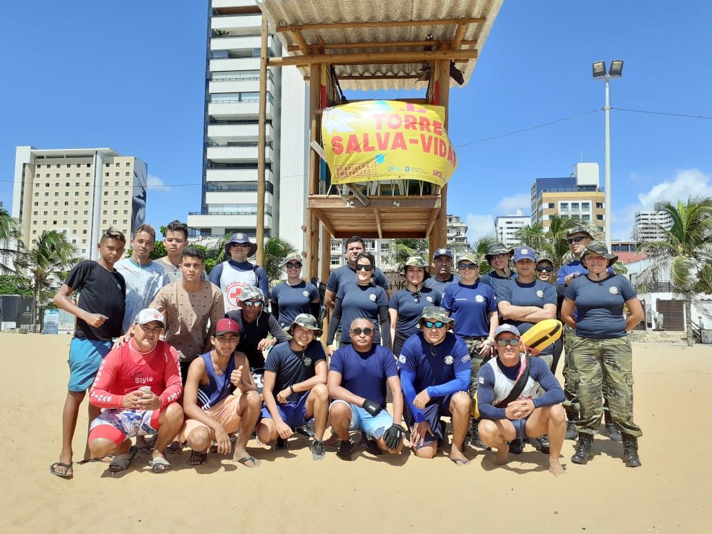 Grupo de pessoas posando em frente a posto de Guarda-Vidas na areia da praia