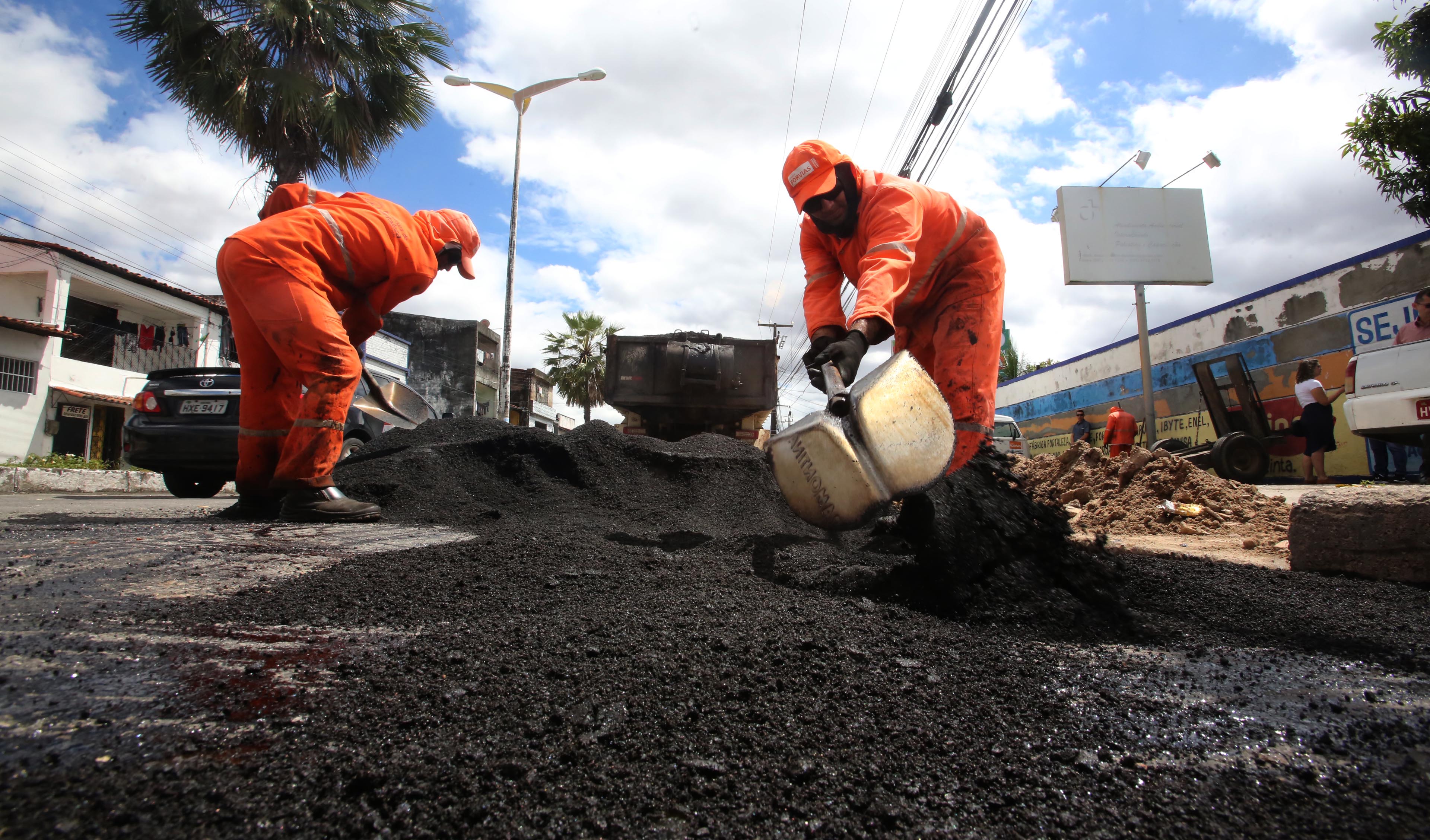 Dois operários mexendo asfalto em obra