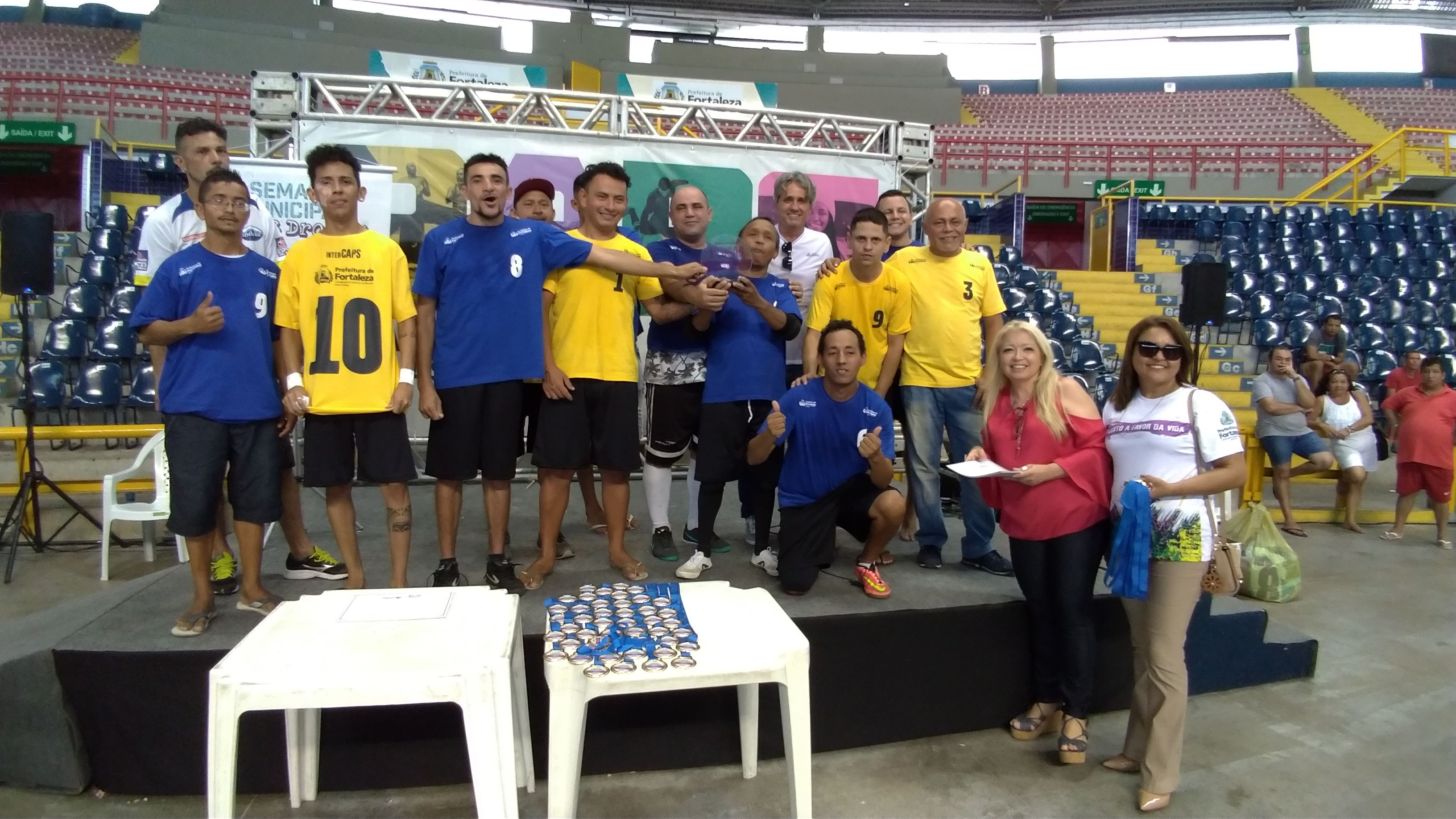 Homens em palco segurando troféus e medalhas