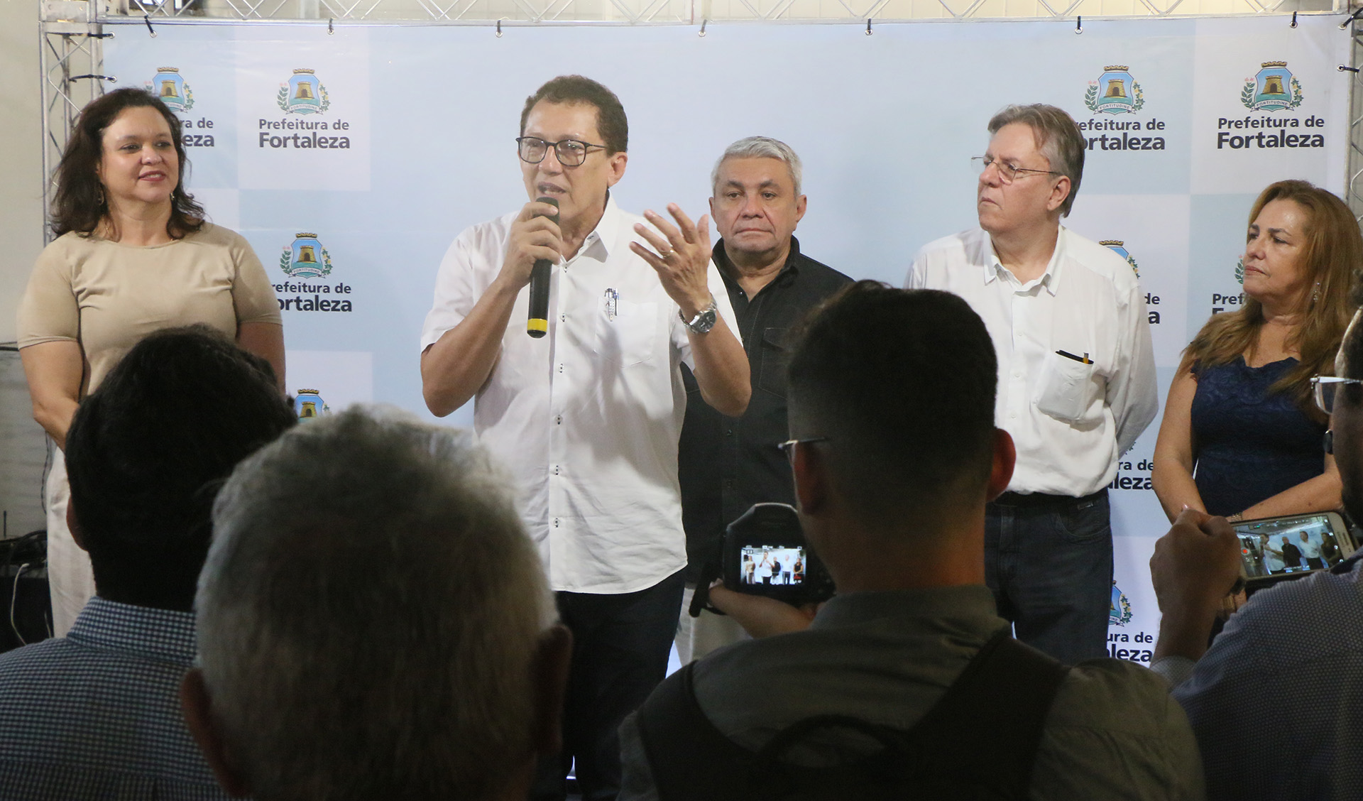 Secretário fala em microfone em cima de palco