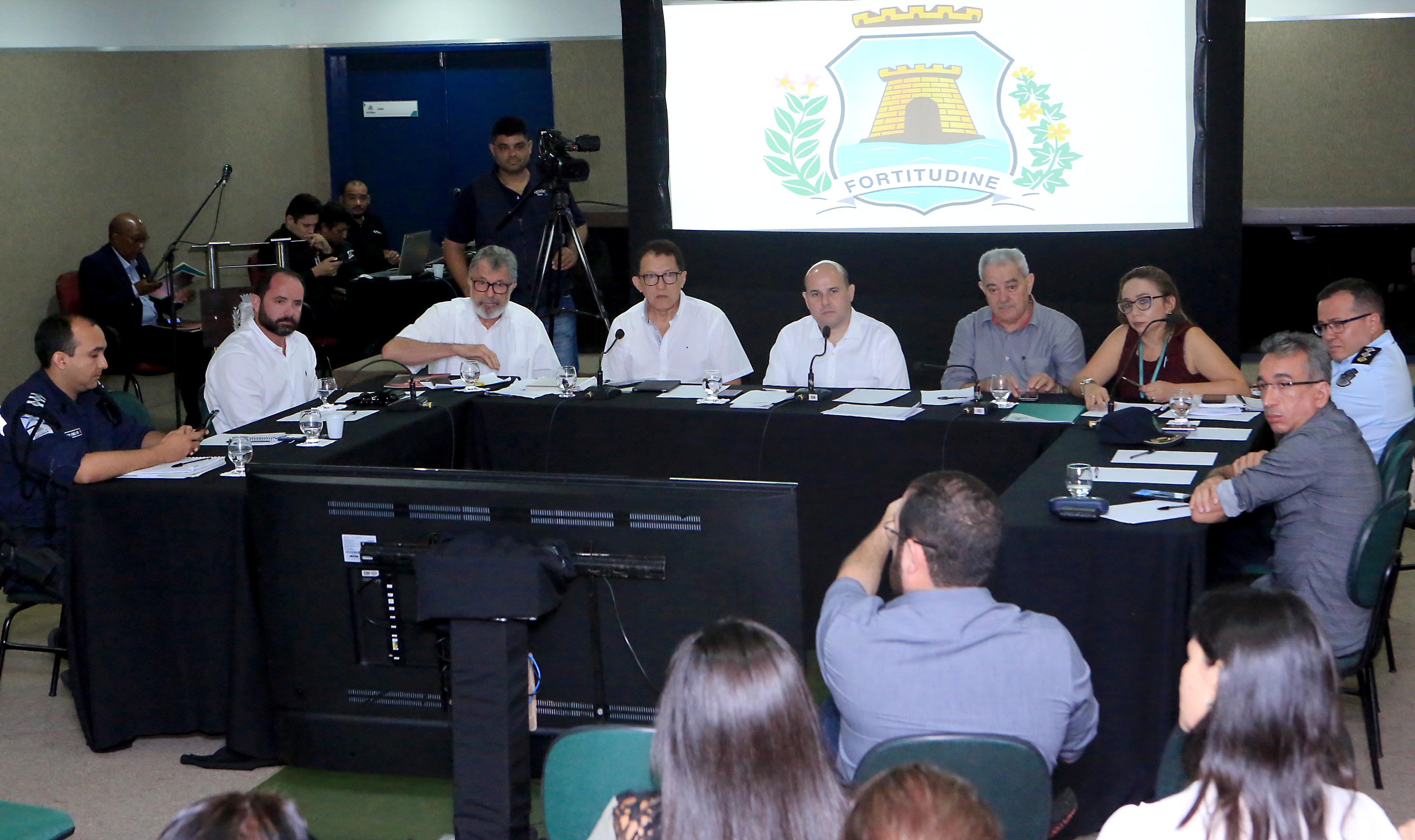 Prefeito em mesa de reunião cercado de pessoas