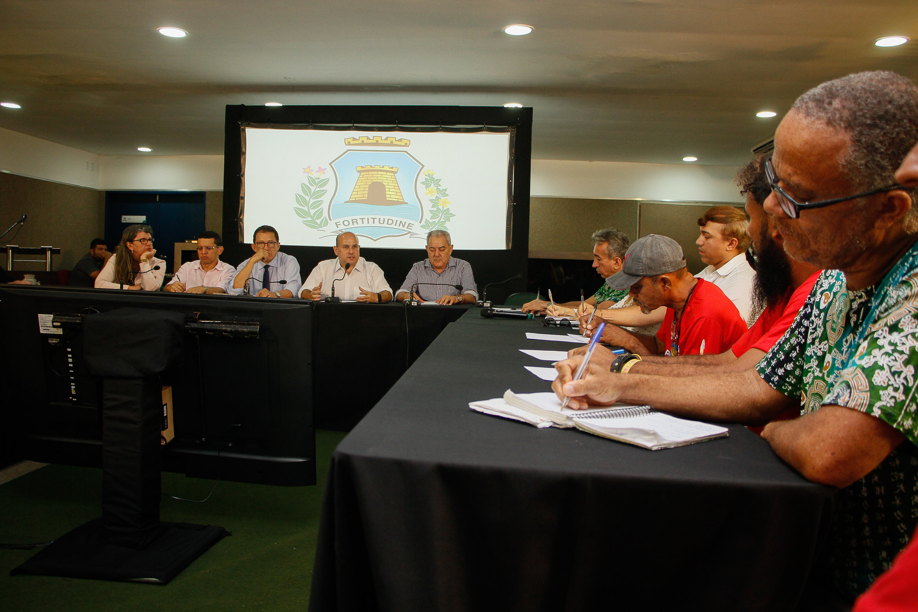 Prefeito fala cercado de pessoas em mesa de reunião