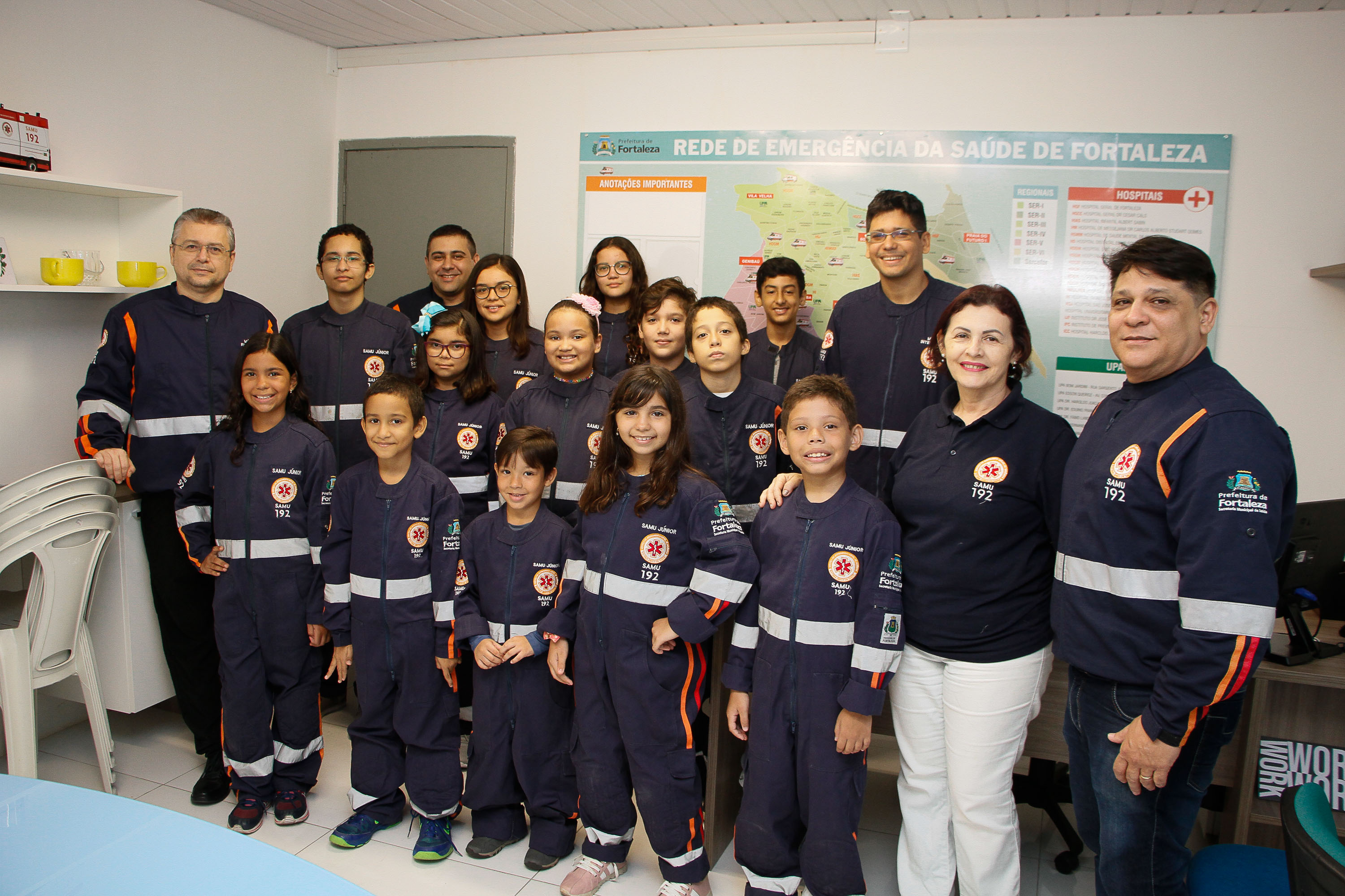 Grupo de instrutores e crianças em pé sorrindo e vestidas com uniforme do Samu