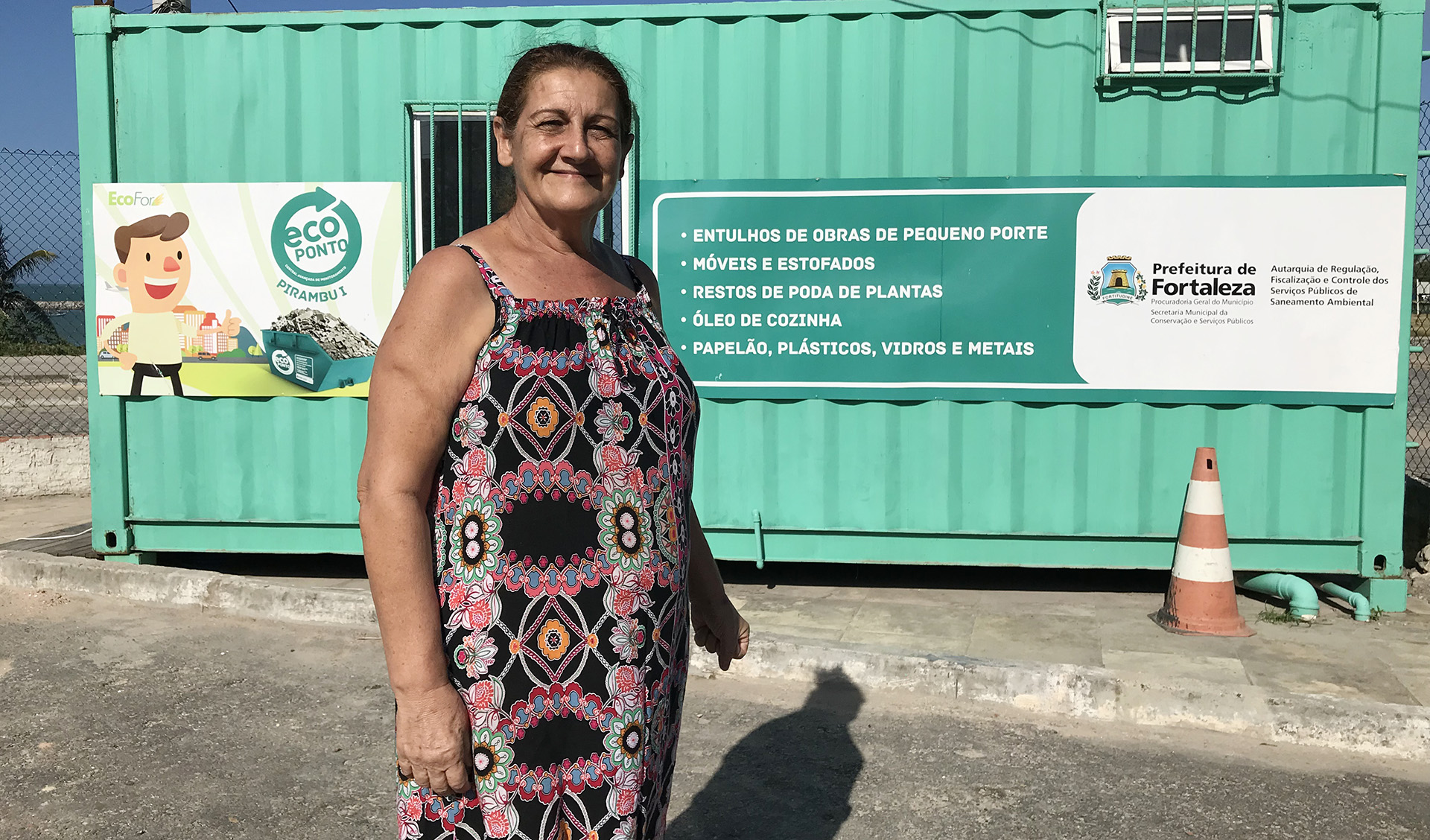 Mulher em pé sorrindo em frente conteiner de Ecoponto