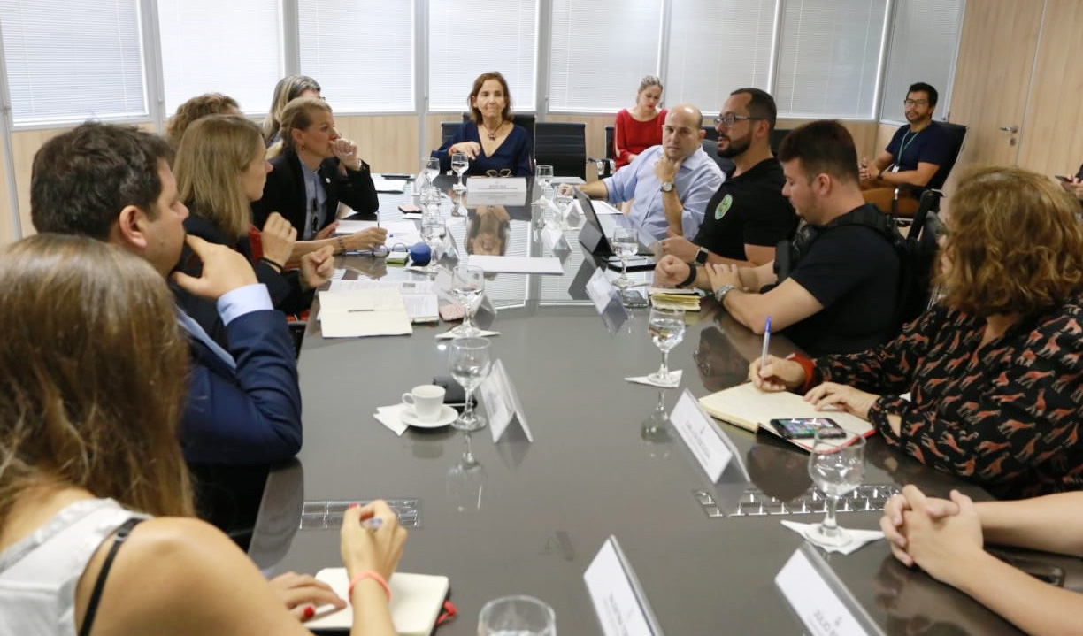 Vice-governadora e prefeito sentados à mesa lado a lado e demais pessoas sentadas ao redor