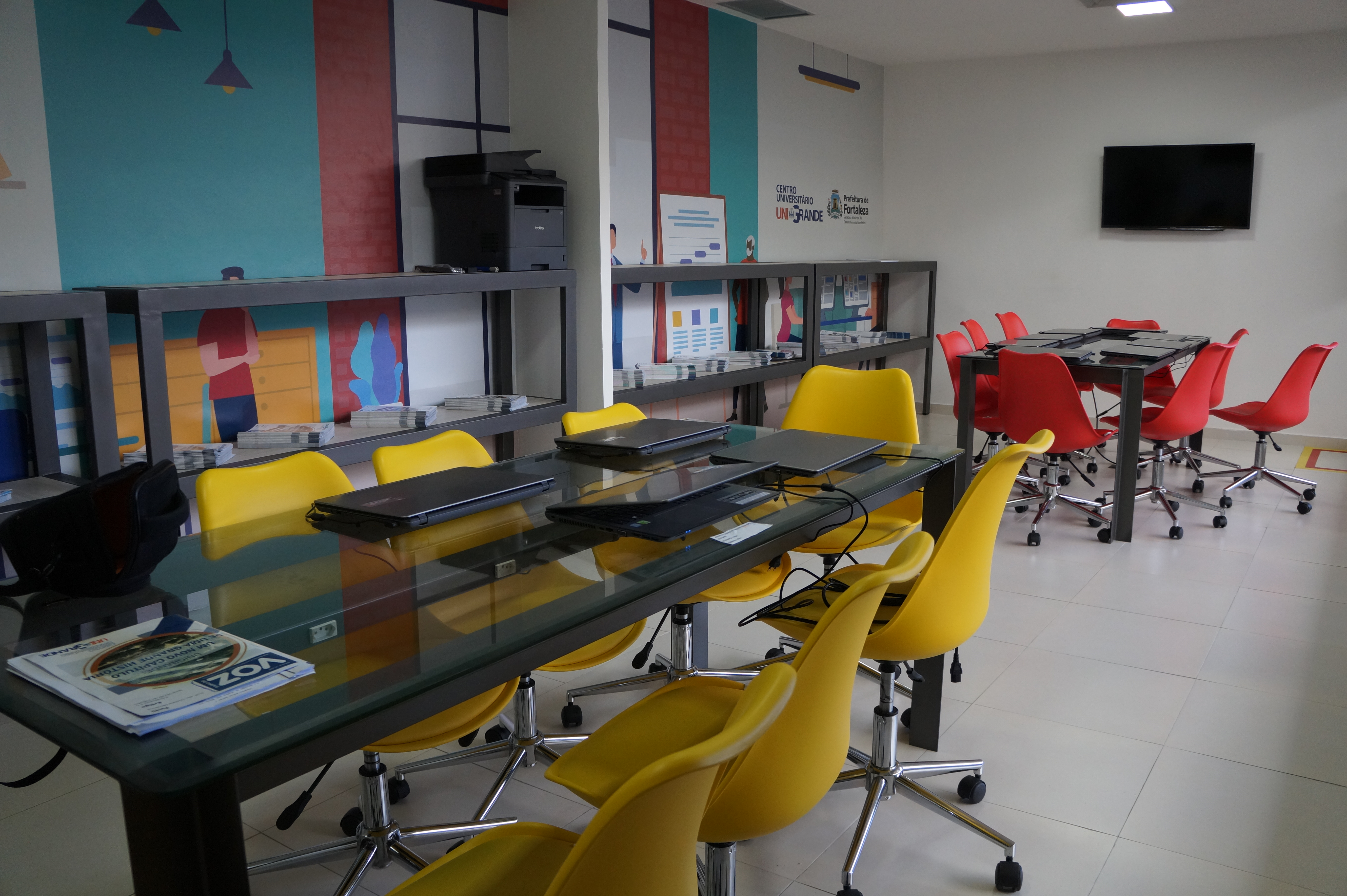 Sala com duas mesas de reunião e cadeiras coloridas ao redor delas