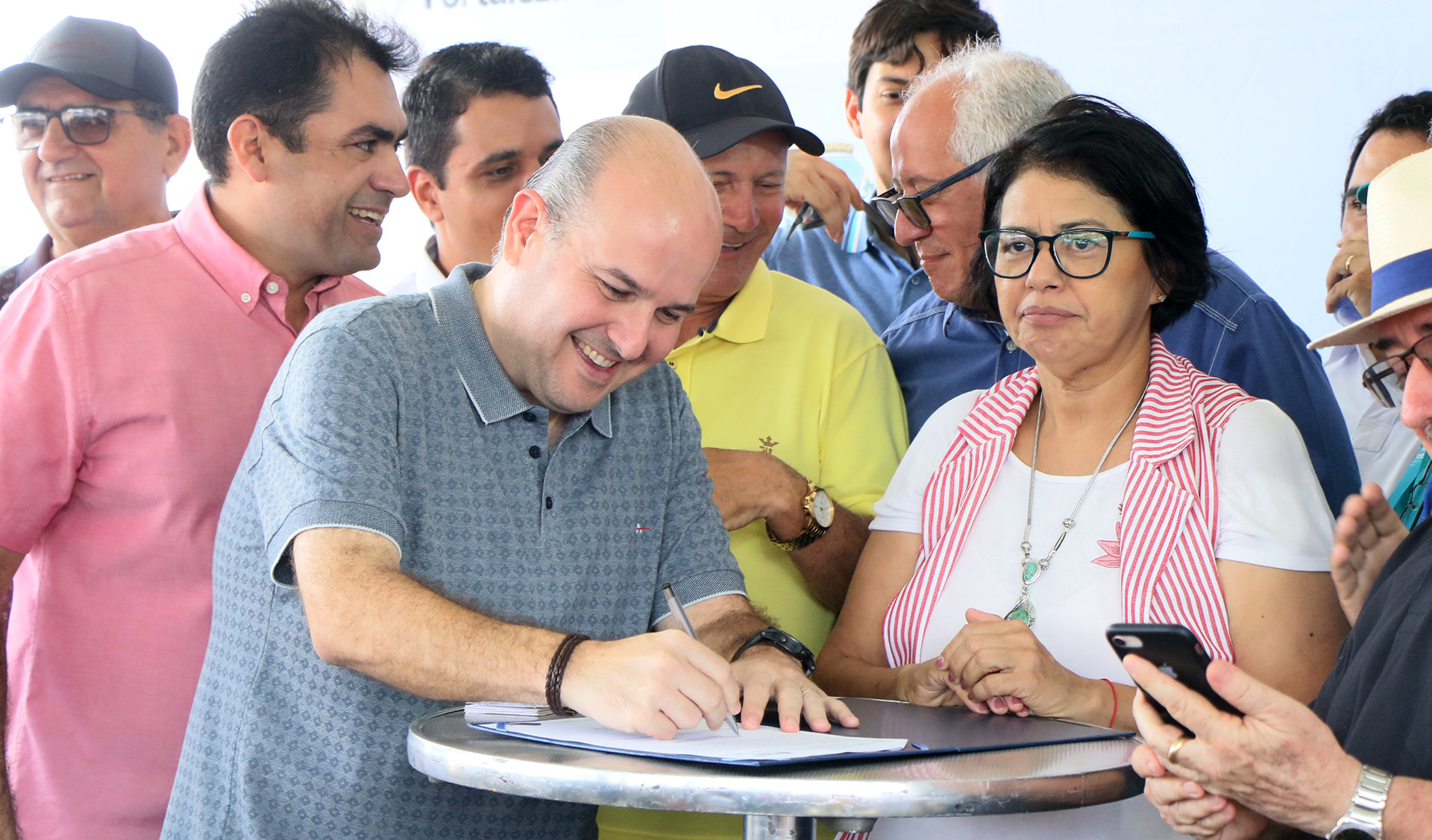 Prefeito assinando documento e pessoas ao redor assistindo