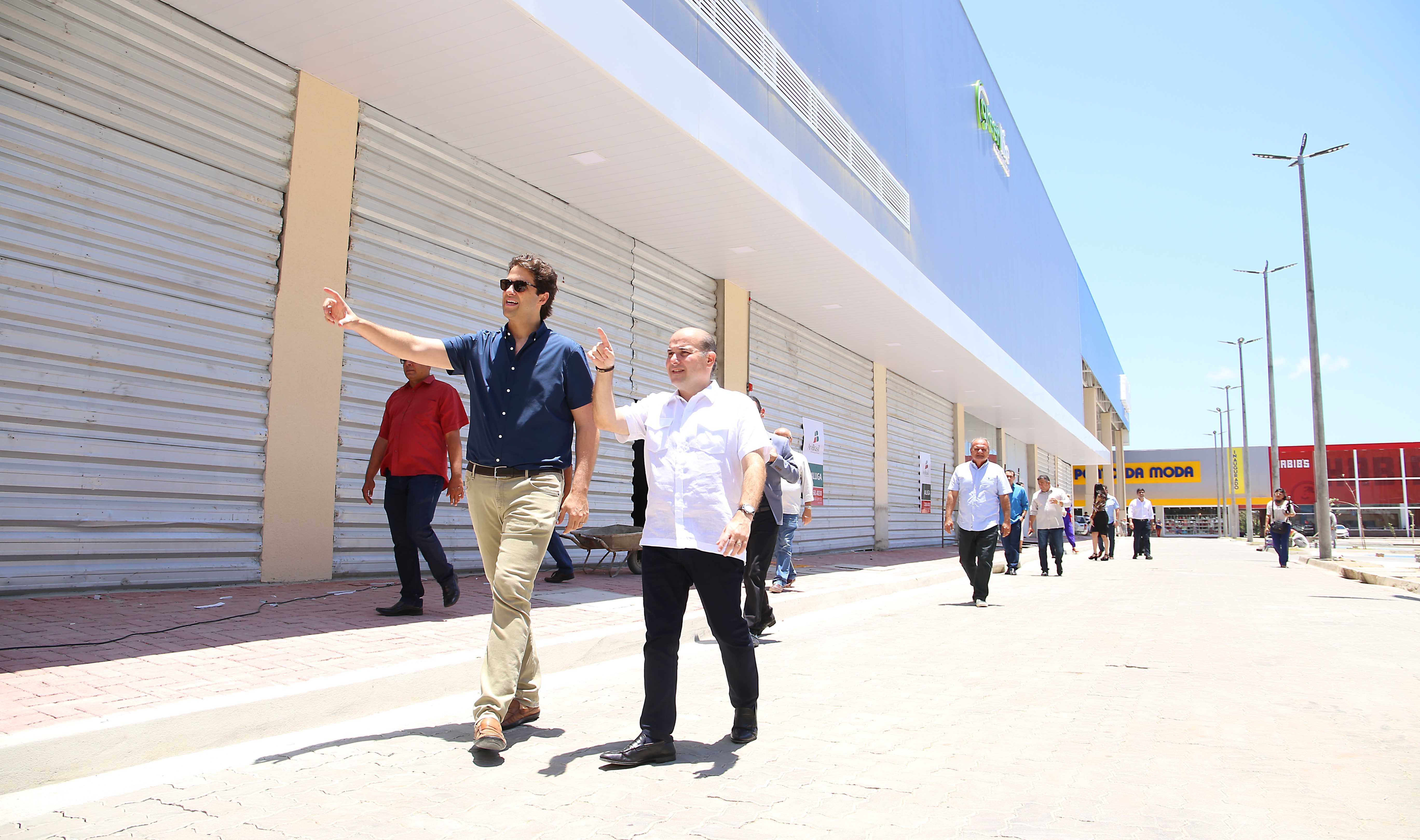 Prefeito caminhando ao lado de rapaz conhecendo área externa de shopping