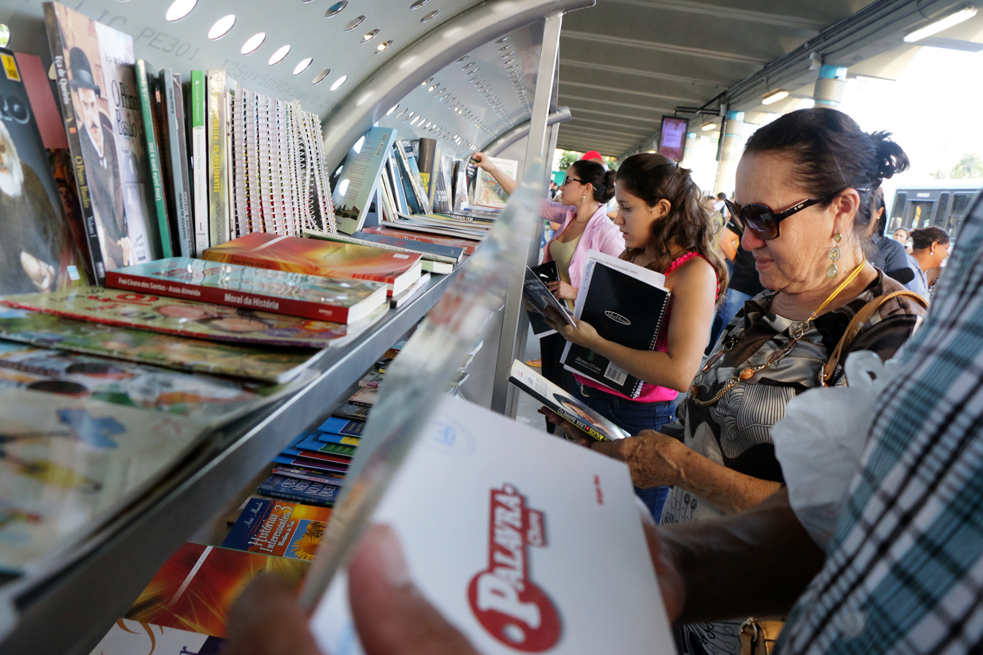 Mulher pega livro exposto nas prateleiras do Terminal Literário