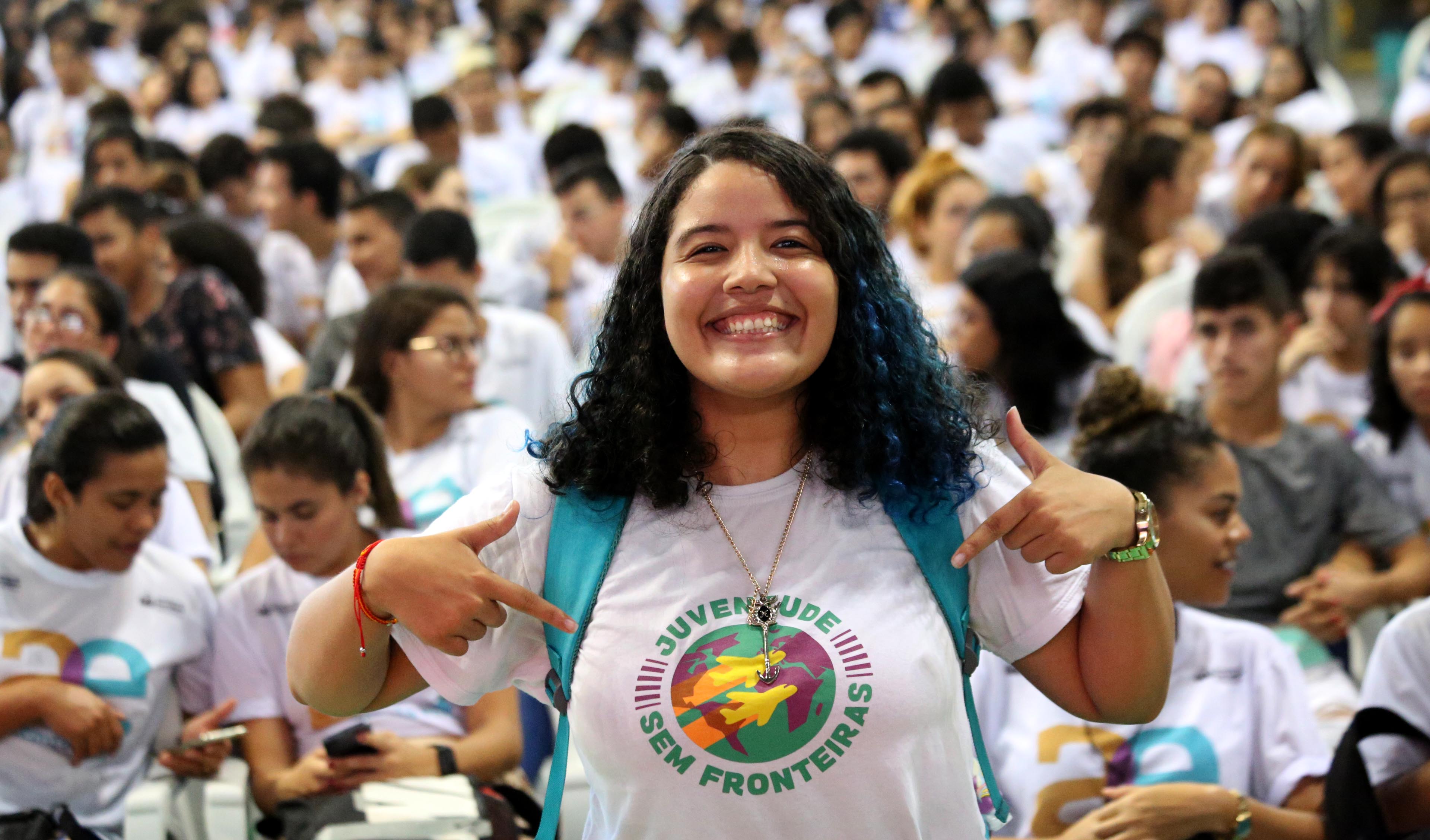 garota sorrindo para a foto e apontando para a camisa que usa do Juventude Sem Fronteiras