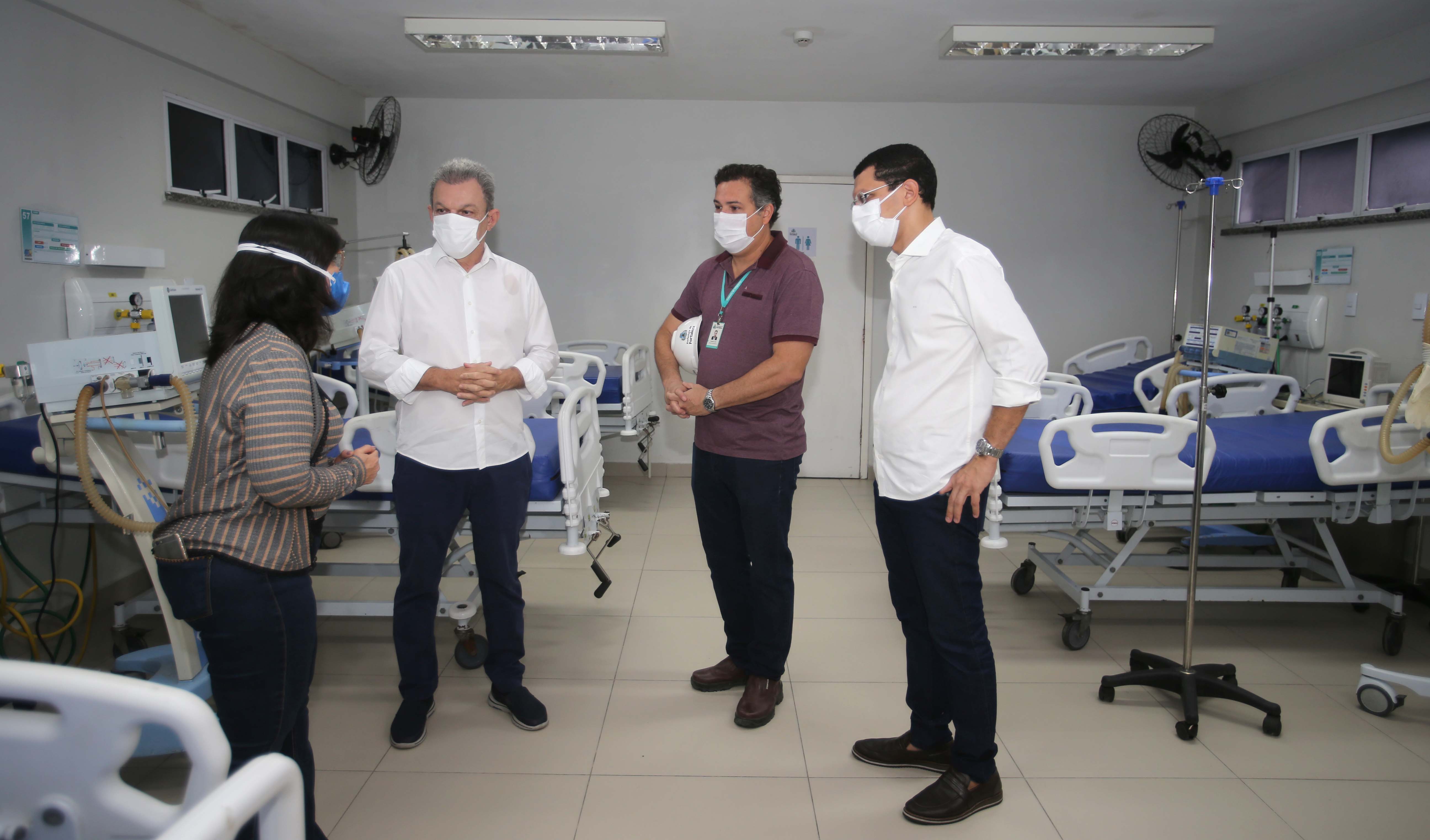 quatro pessoas com máscara convesam dentro de uma enfermaria de hospital que está sem pacientes