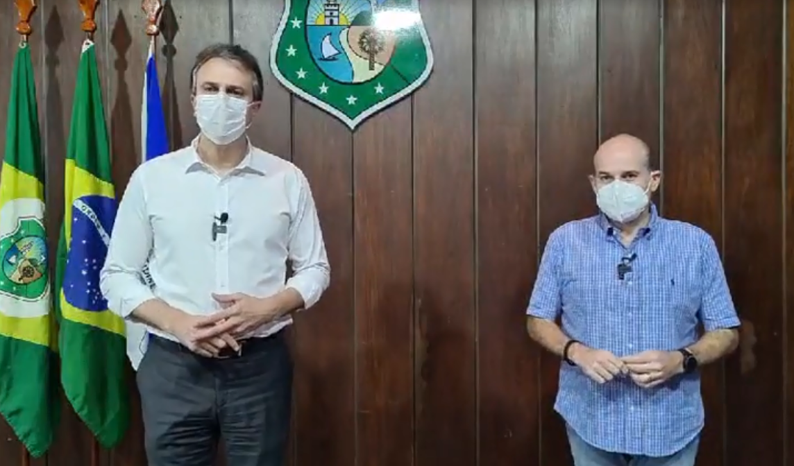 governador e prefeito lado a lado posando para a foto, usando máscaras e com brasão do estado do Ceará e bandeiras ao fundo