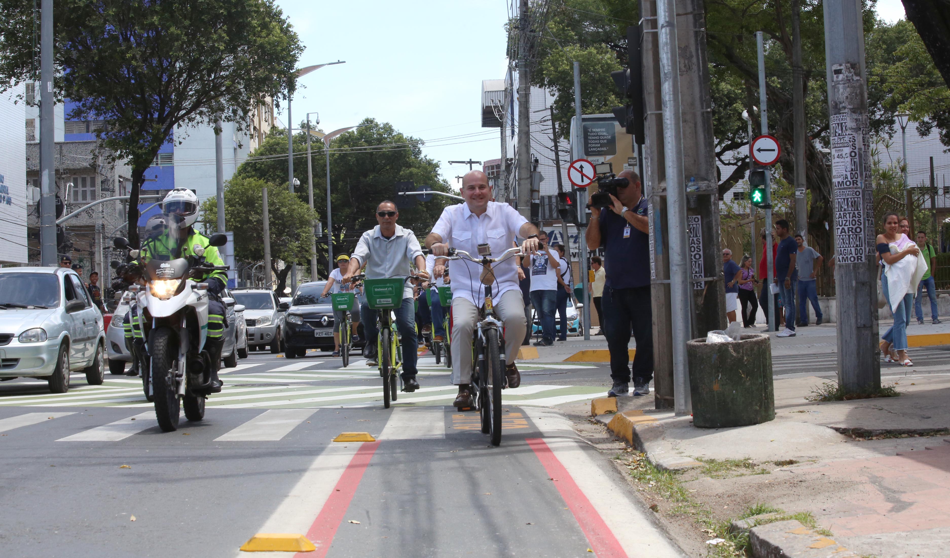 prefeito andando de bicicleta por avenida e pessoas acompanhando ao lado