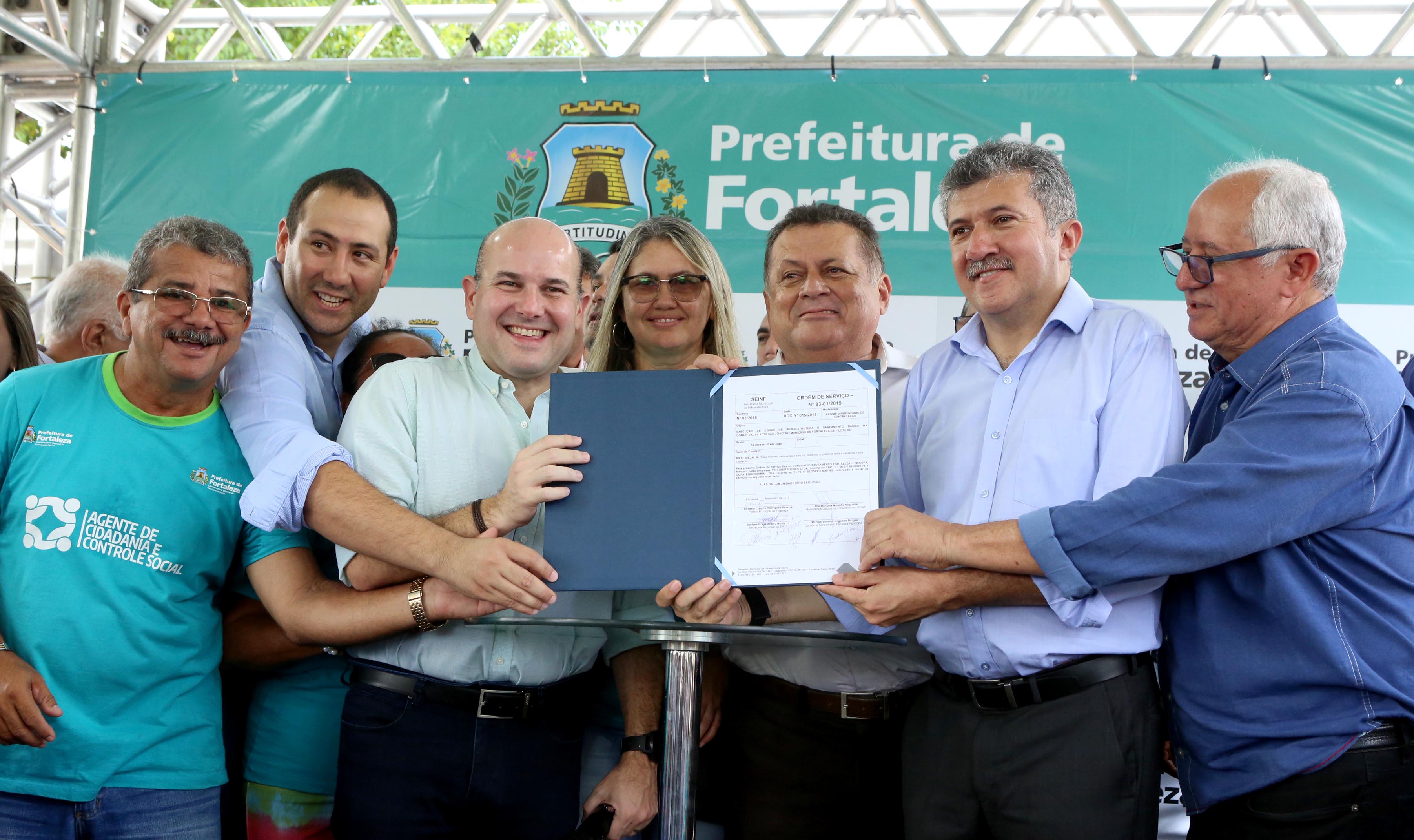 prefeito e outras pessoas segurando documento e sorrindo para a foto