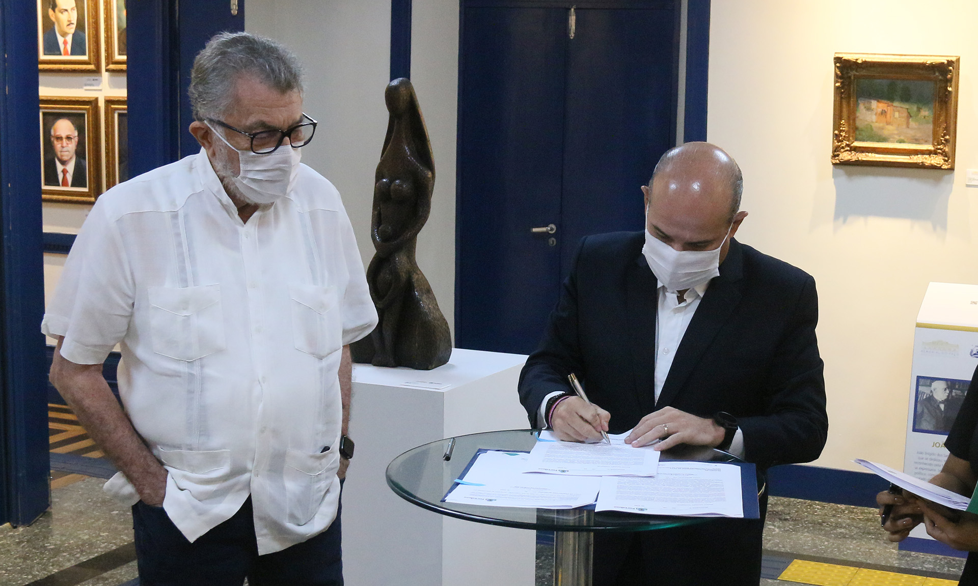 Eudoro Santana ao lado do prefeito, que assina um documento em cima de uma mesa