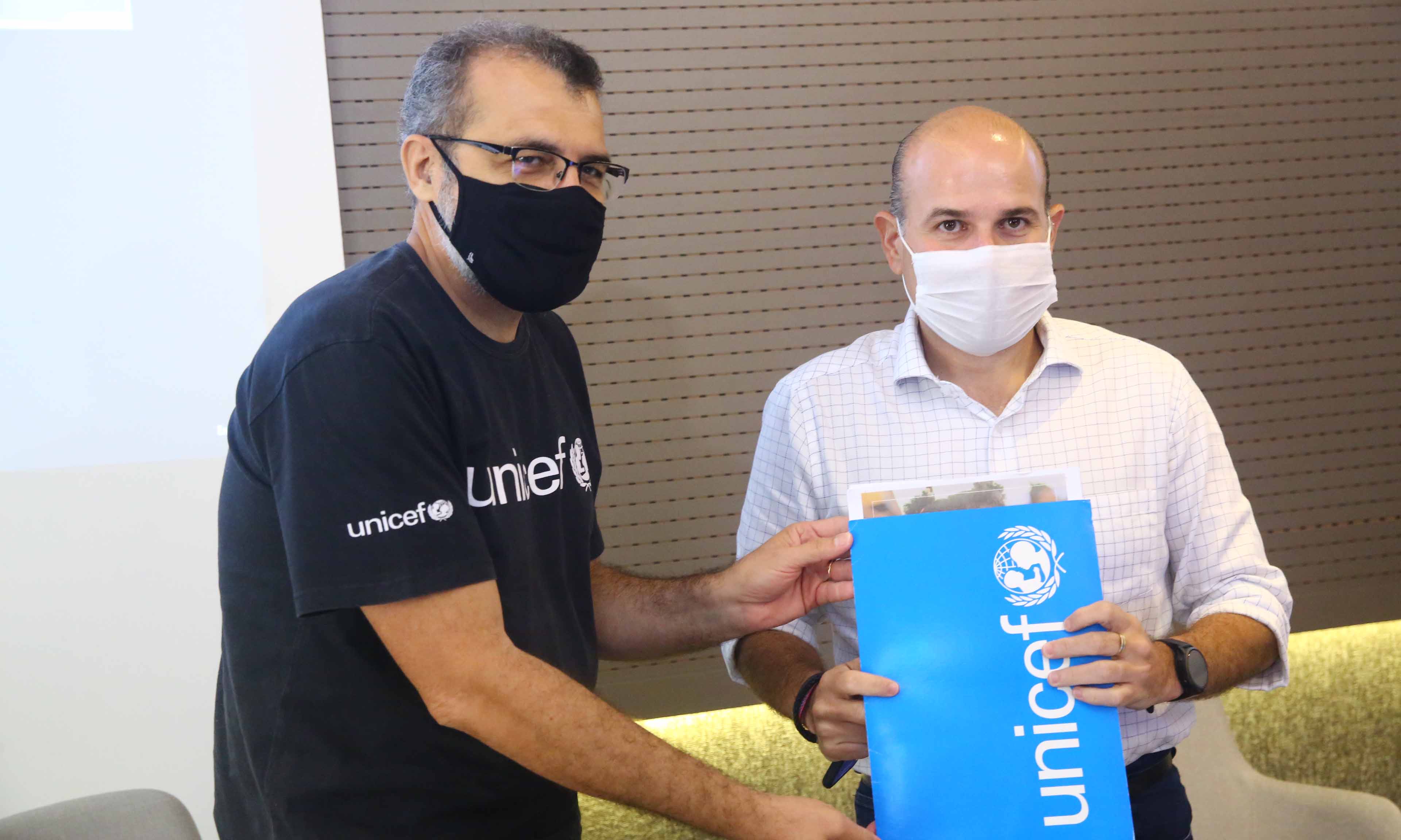 Rui Aguiar e prefeito, ambos de máscara posando para a foto. Prefeitura segura pasta com marca da Unicef