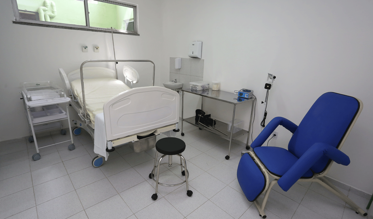 sala de hospital com maca, poltrona de acompanhante, mesa lateral, berço e acessórios