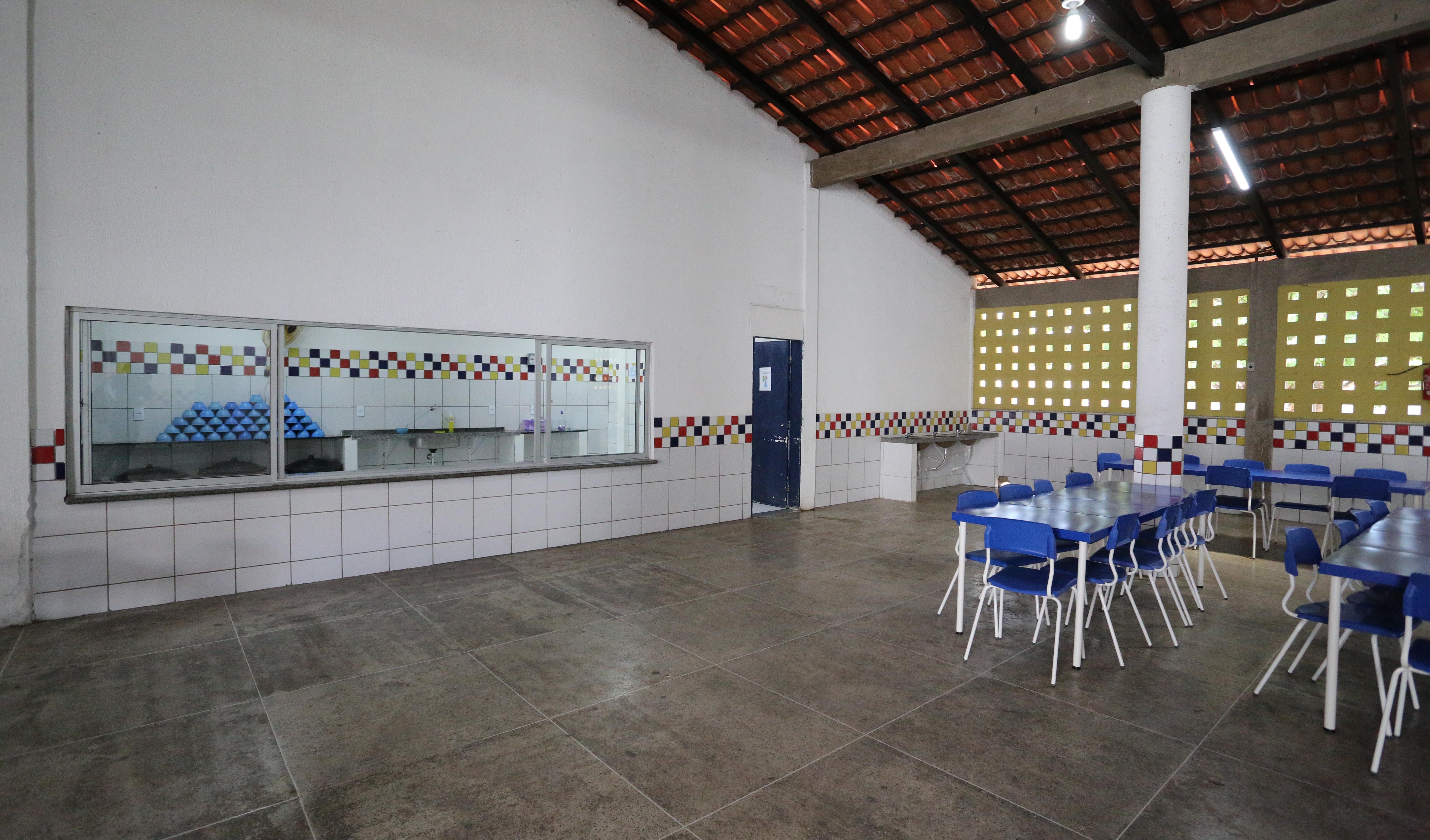 a imagem mostra o refeitório da escola com várias mesas e cadeiras