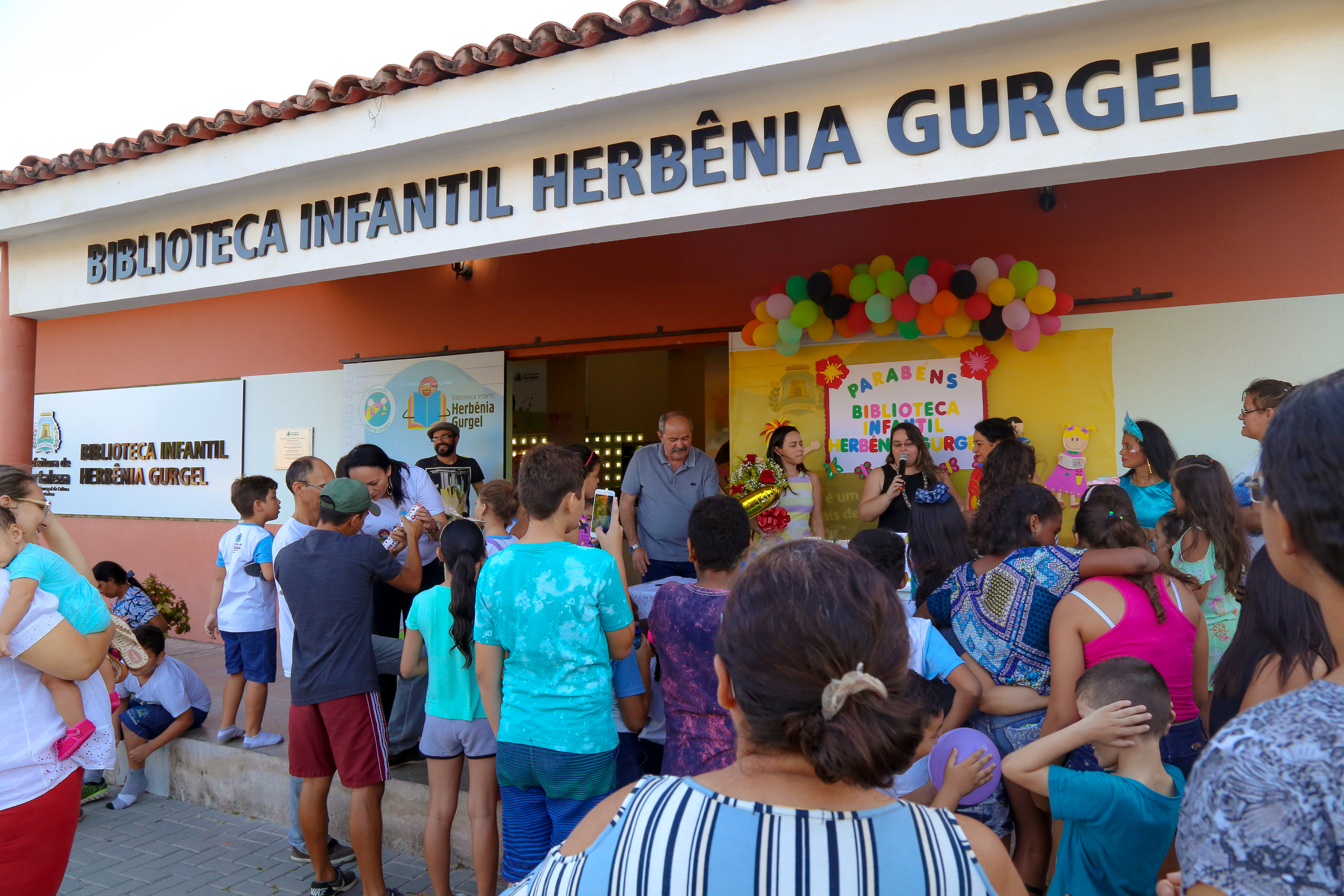Pais, crianças e jovens em frente à faixada da Biblioteca Herbênia Gurgel
