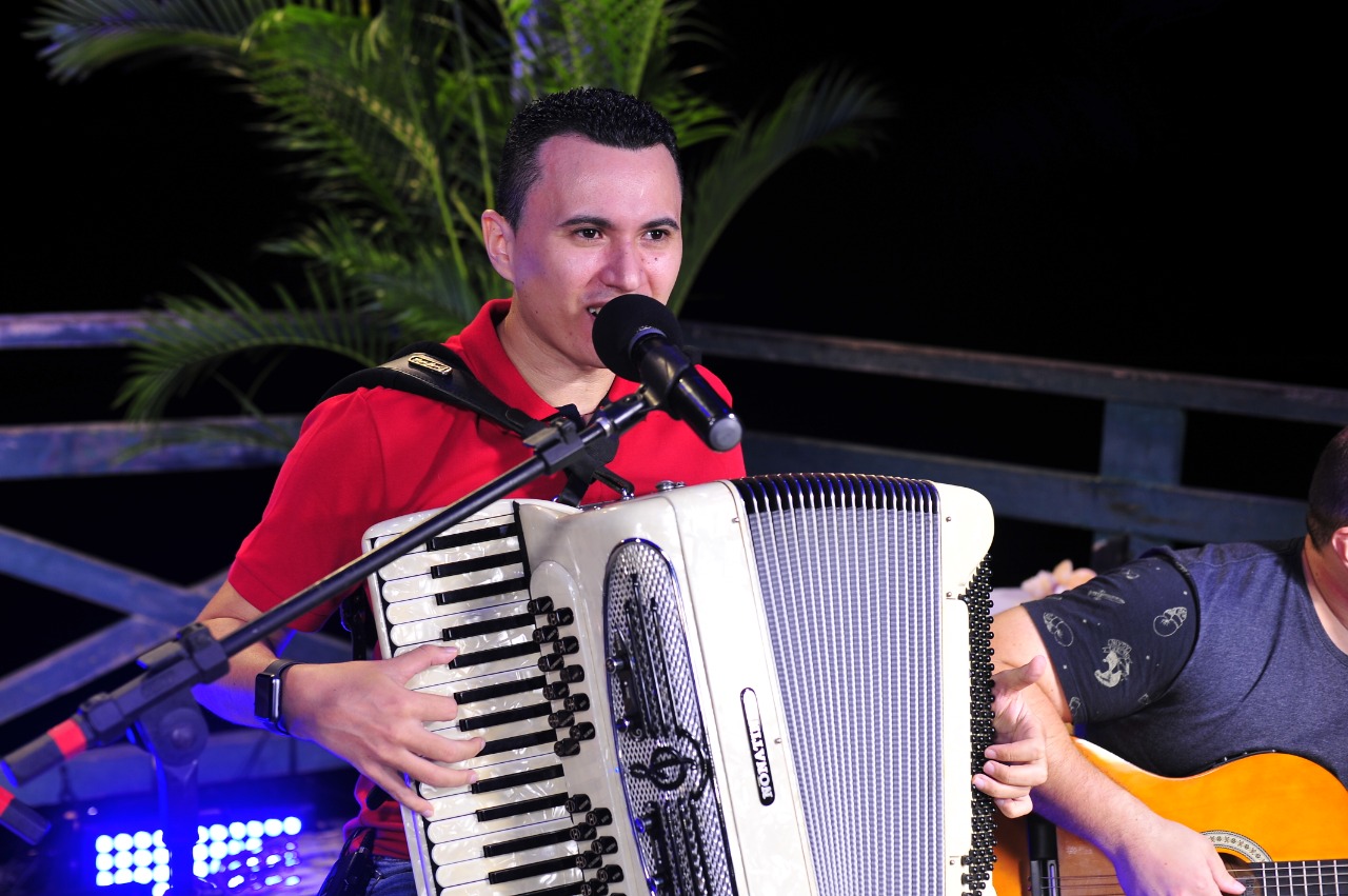 Músico Nonato Lima cantando no microfone e segurando um acordeon
