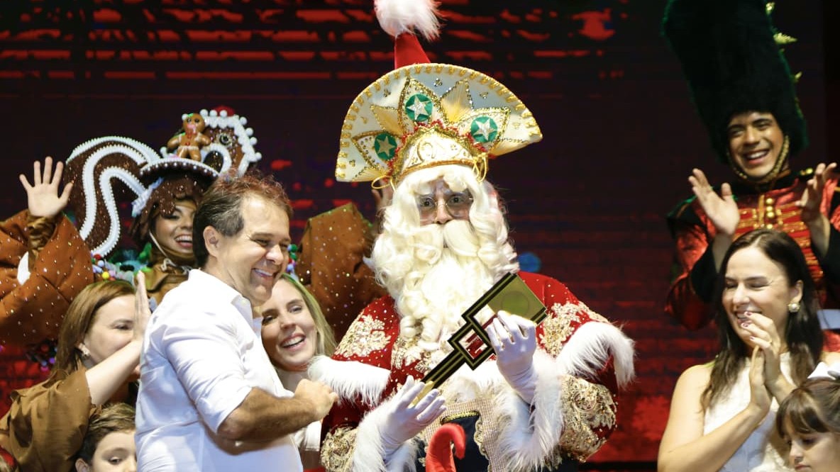 Prefeito Evandro Leitão entrega a chave da cidade para o Papai Noel na abertura do Natal de Luz. Eles estão em cima do palco, segurando uma grande chave.