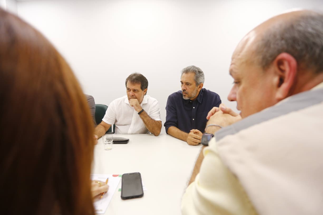 A imagem mostra reunião de gestores em torno de uma mesa, prefeito e governador aparecem em destaque