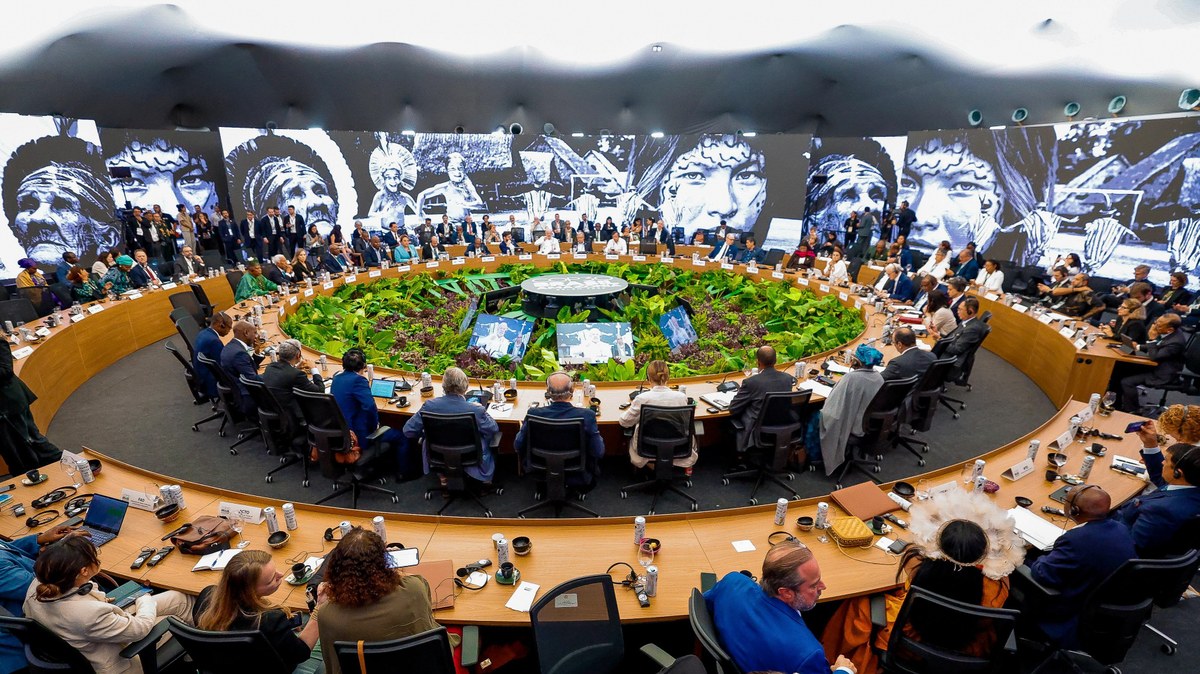 A foto mostra centenas de pessoas reunidas em torno de uma mesa redonda em um evento diplomático