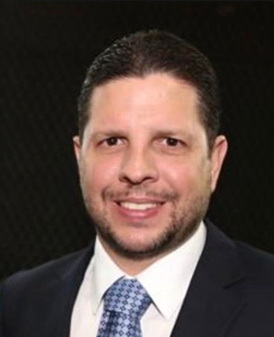 Homero Silva posa para a foto de terno preto, camisa branca e gravata azul