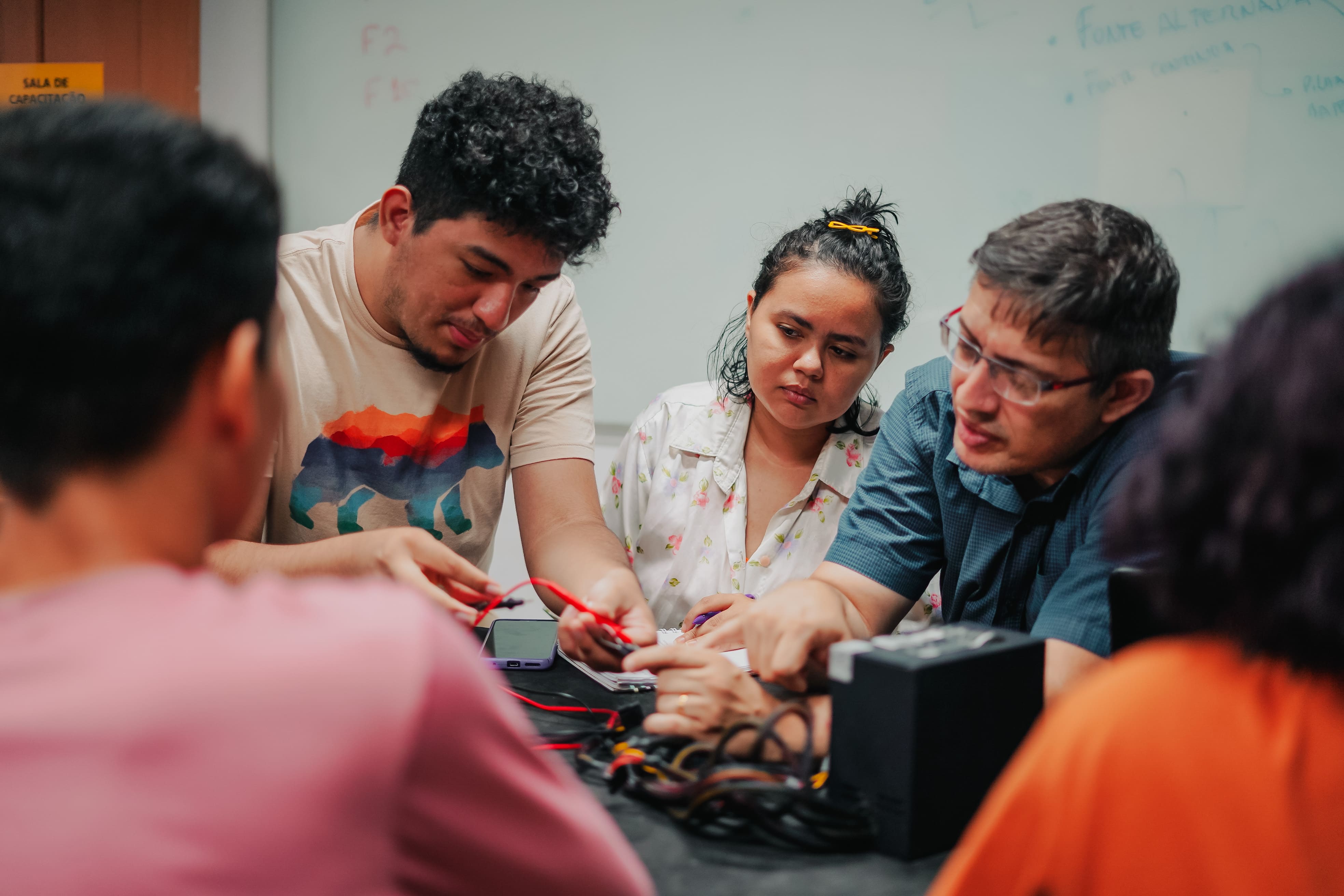 Alunos do curso ao redor de mesa aprendendo com o professor. 