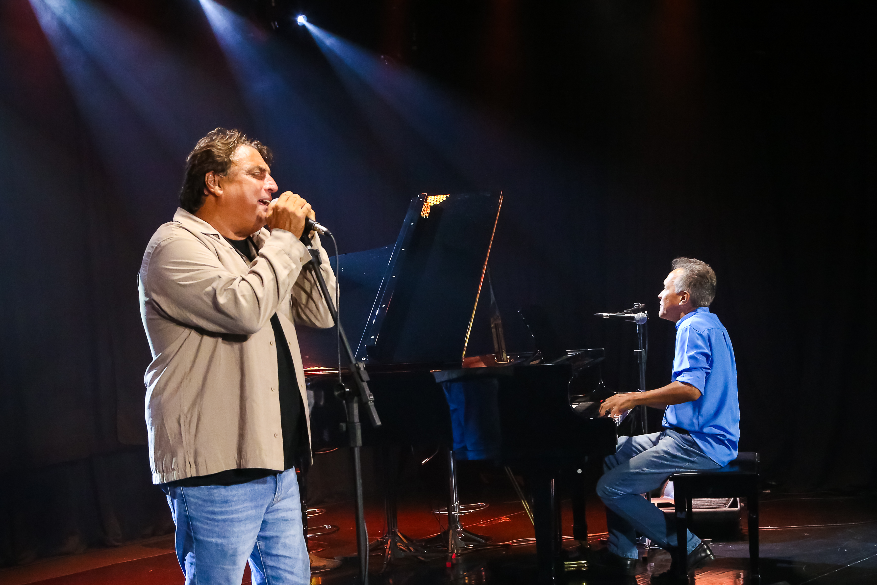 dois homens cantando, um deles toca um piano de cauda