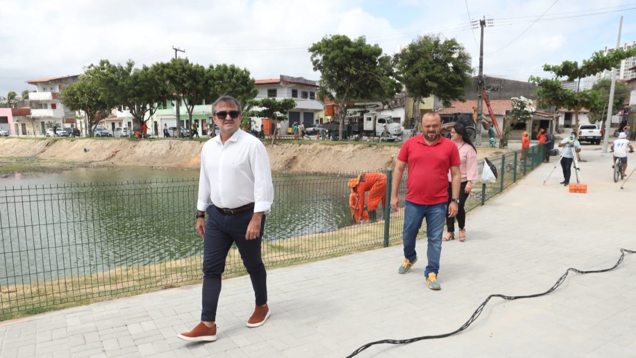 grupo de pessoas caminhando em um calçadão à margem de uma lagoa