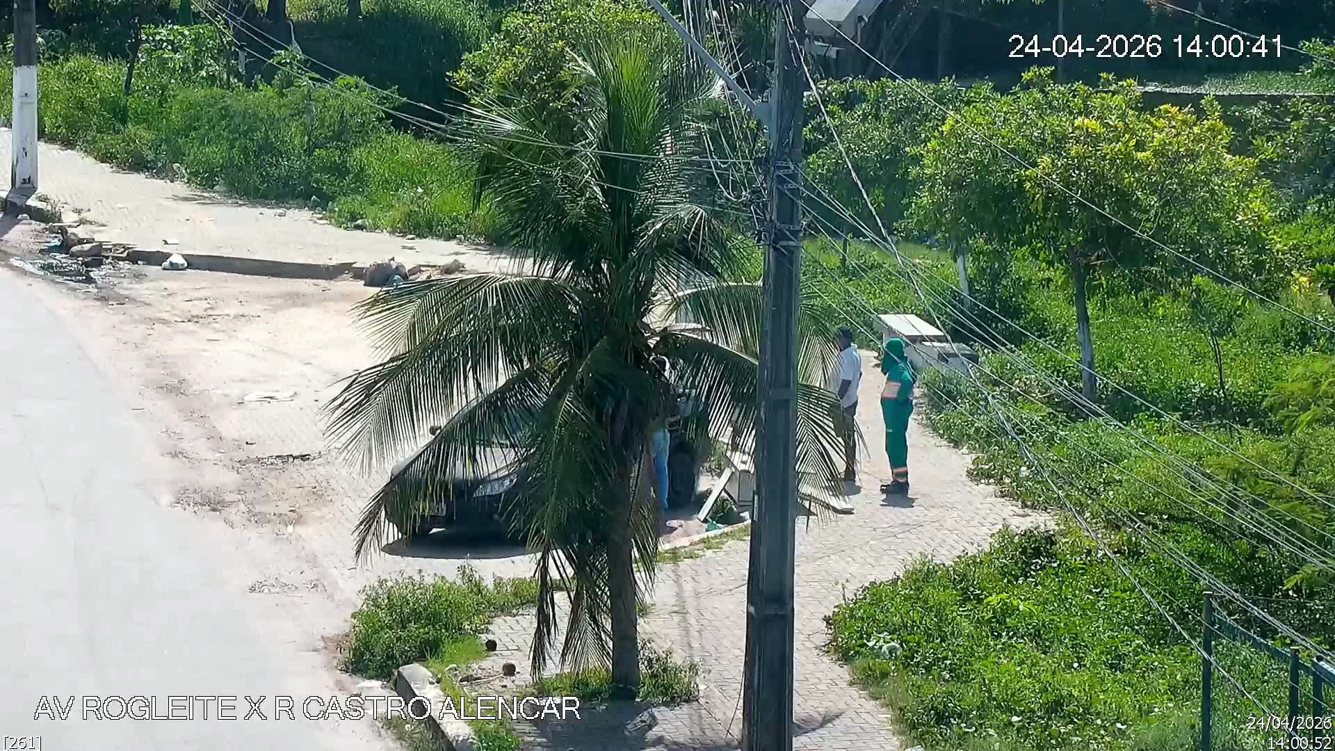 Imagem mostra veículo parado em calçada enquanto proprietário descarta resíduo de forma irregular ao lado de agente de limpeza urbana